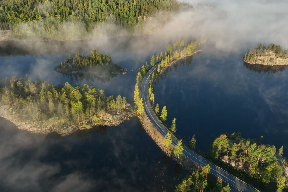 Ilmasta käsin kuvattu järvimaisema, jonka keskellä kaartaa autotie